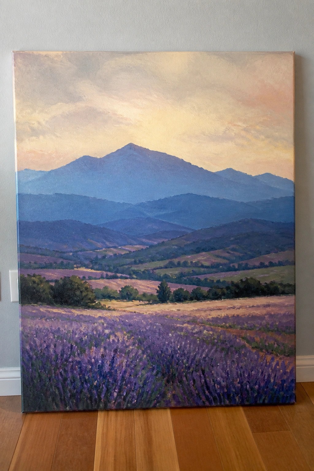 Lavender fields stretch toward layered blue mountains under a pastel sunset sky