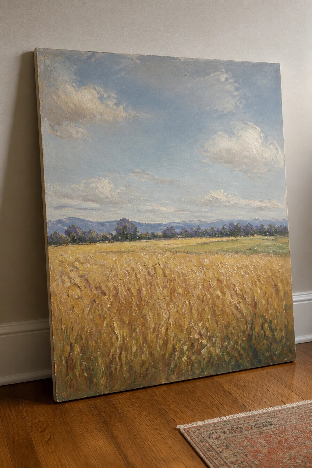 Large landscape painting of golden wheat field leaning against wall on wood floor