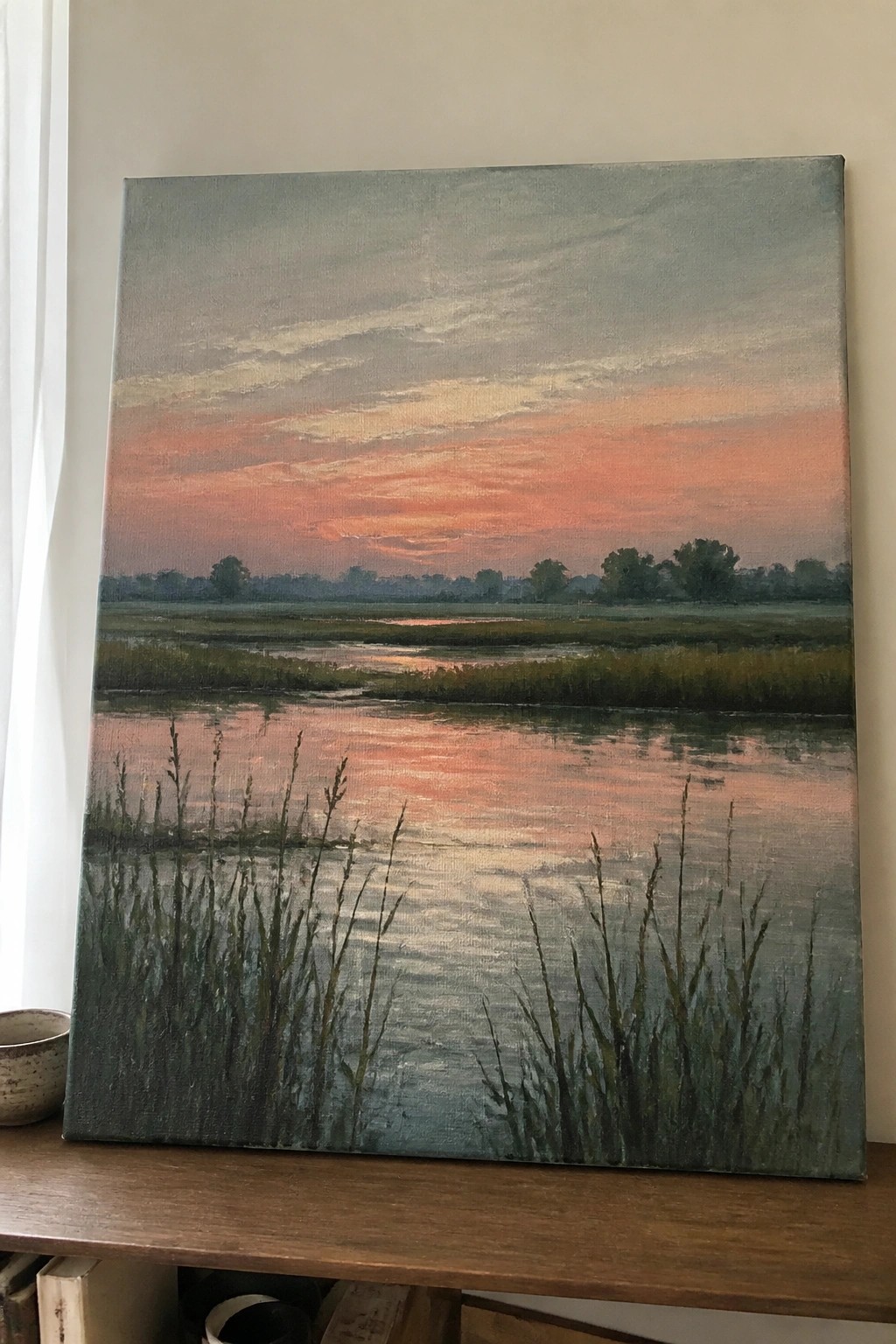 Painting of orange-pink sunset reflecting over marsh with tall reeds in foreground.