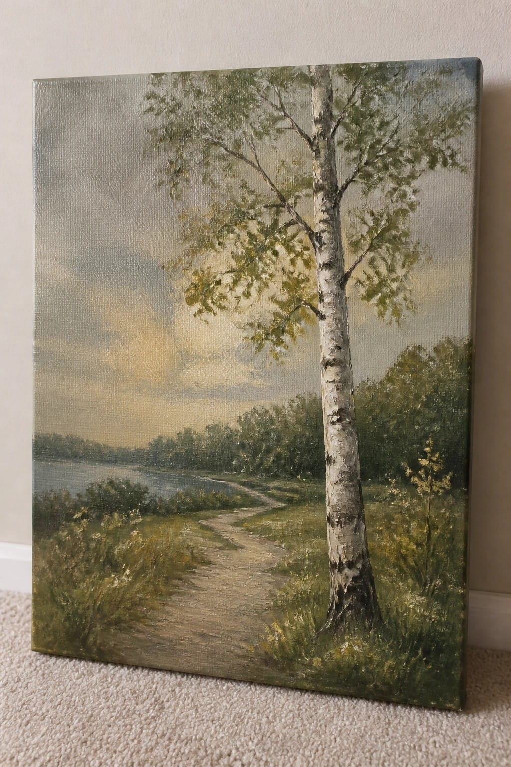 Oil painting of birch tree by winding path leading toward lake under cloudy sky.