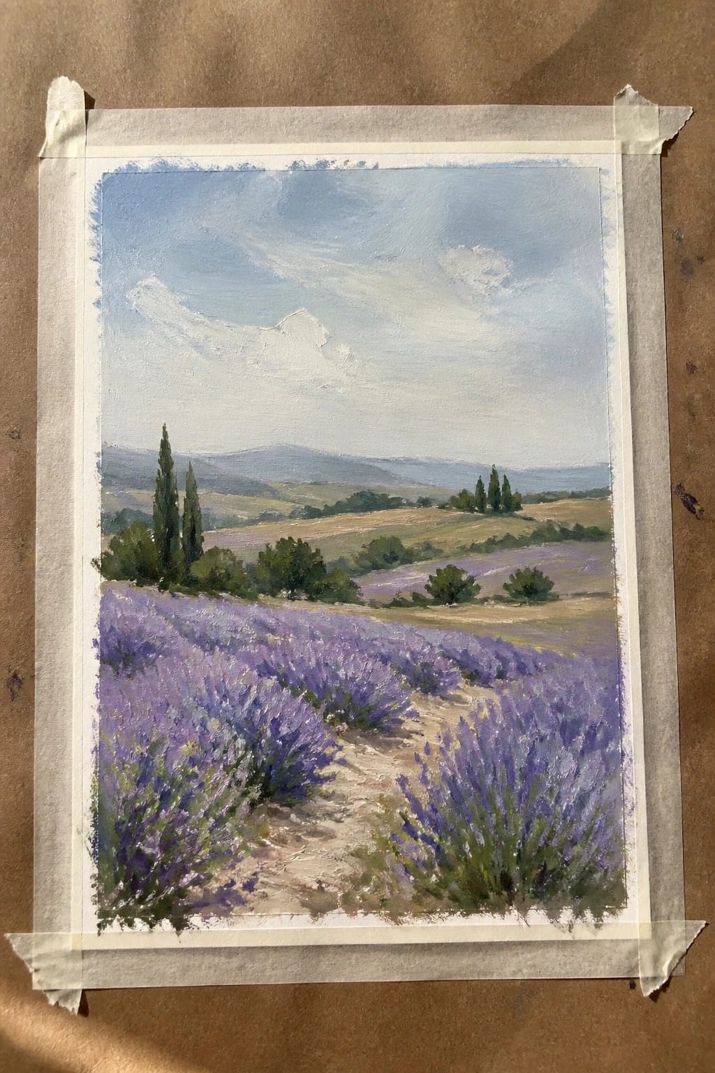 Painting of purple lavender fields with dirt path, trees, and rolling hills under blue sky
