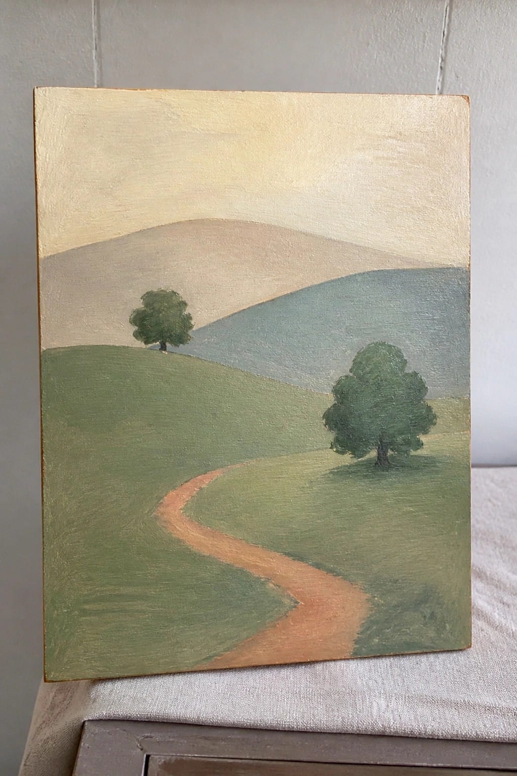 Winding path curves through rolling green hills with two trees under pale sky