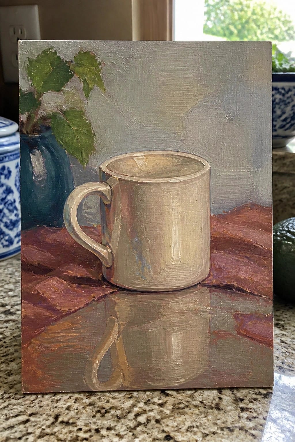 Metallic cup with reflection on reddish cloth beside blue vase with green leaves.