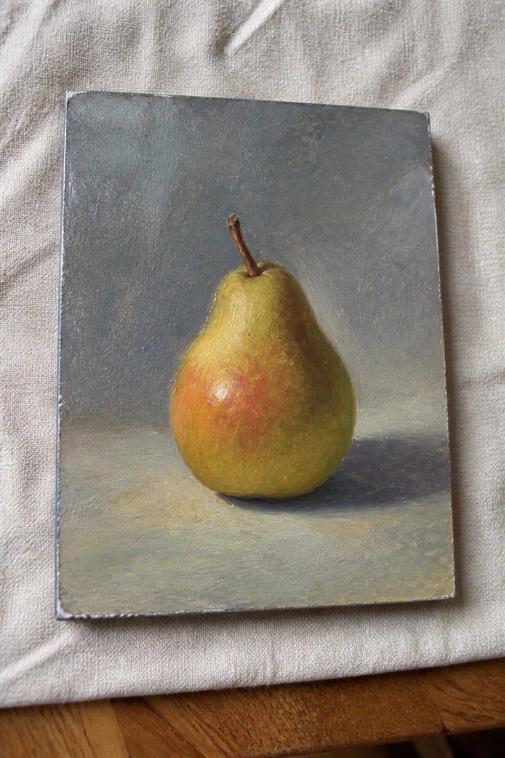 Realistic still life painting of a pear on canvas resting on white cloth