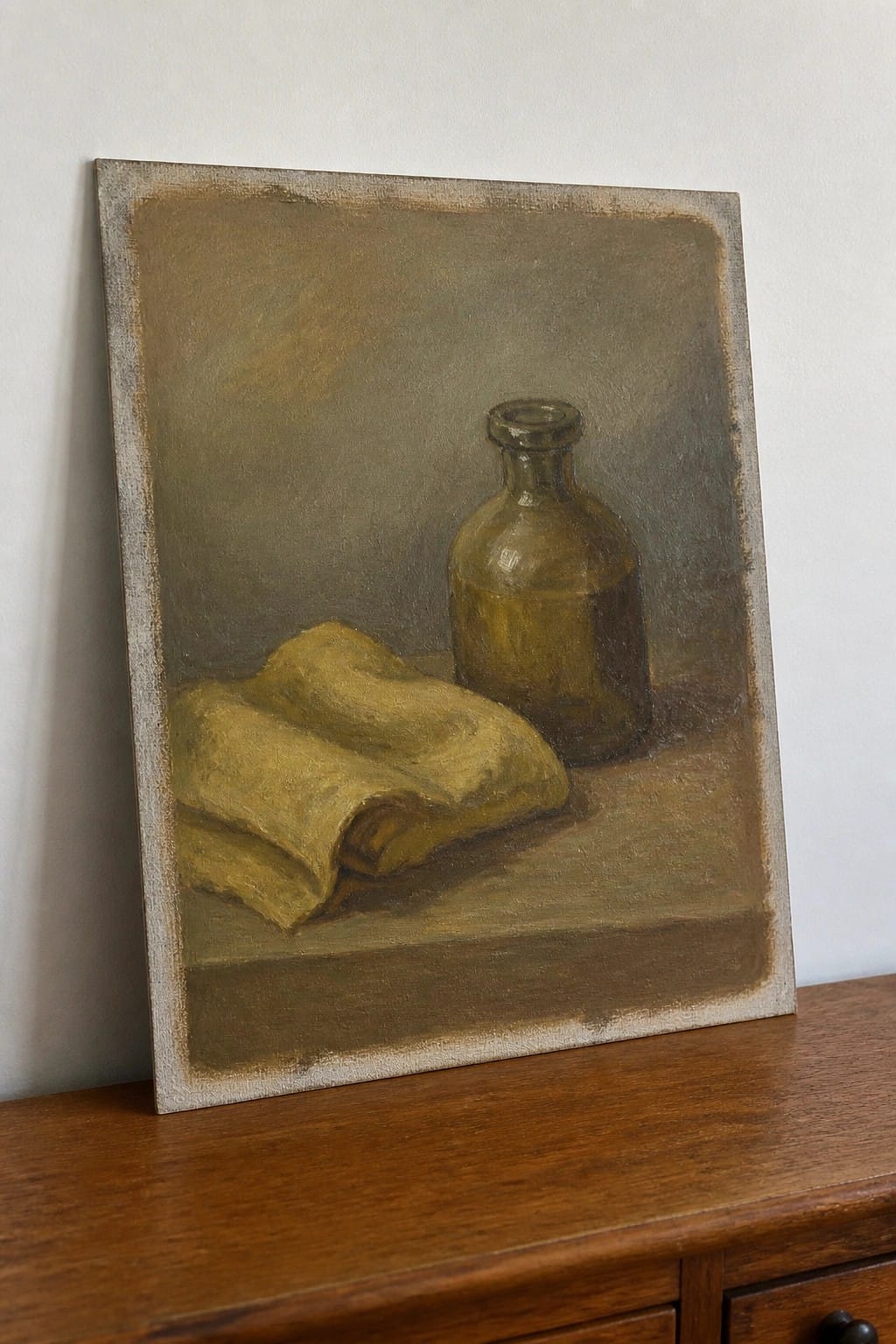 Still life painting of a brown glass bottle and folded yellow cloth on a surface.
