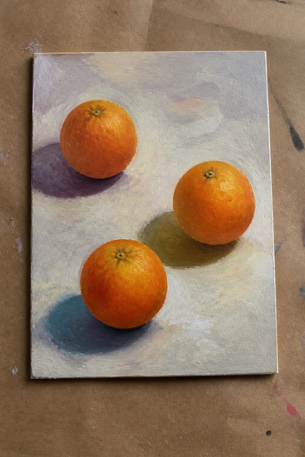 Three oranges with purple, blue, and green shadows on a gray canvas