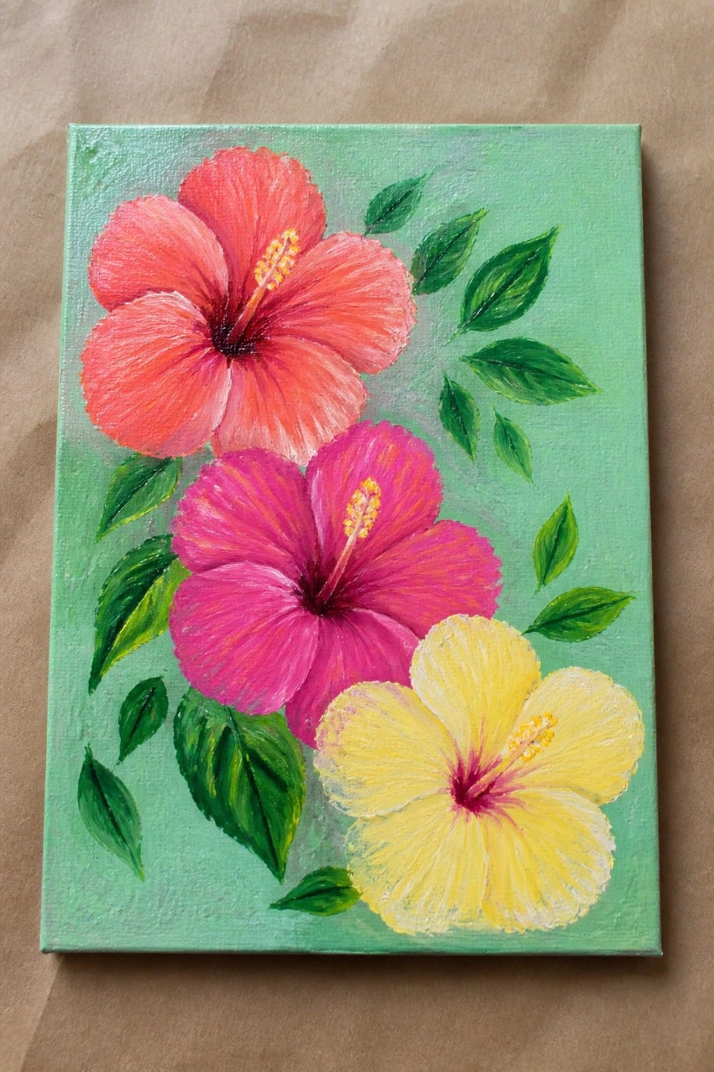 Three vibrant hibiscus flowers in red, pink, and yellow with green leaves on canvas