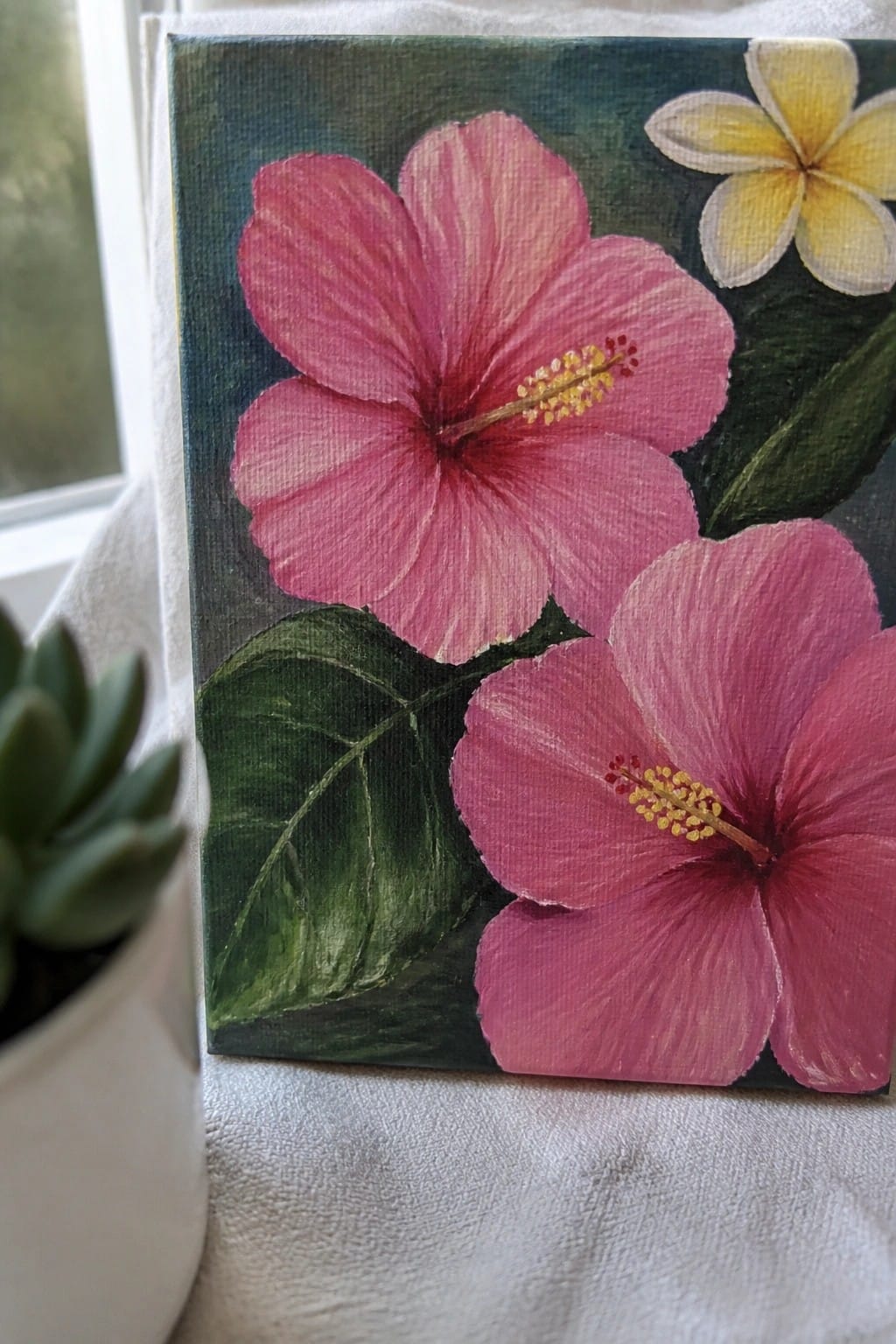 Vibrant acrylic painting of two pink hibiscus flowers and yellow plumeria with green leaves on canvas