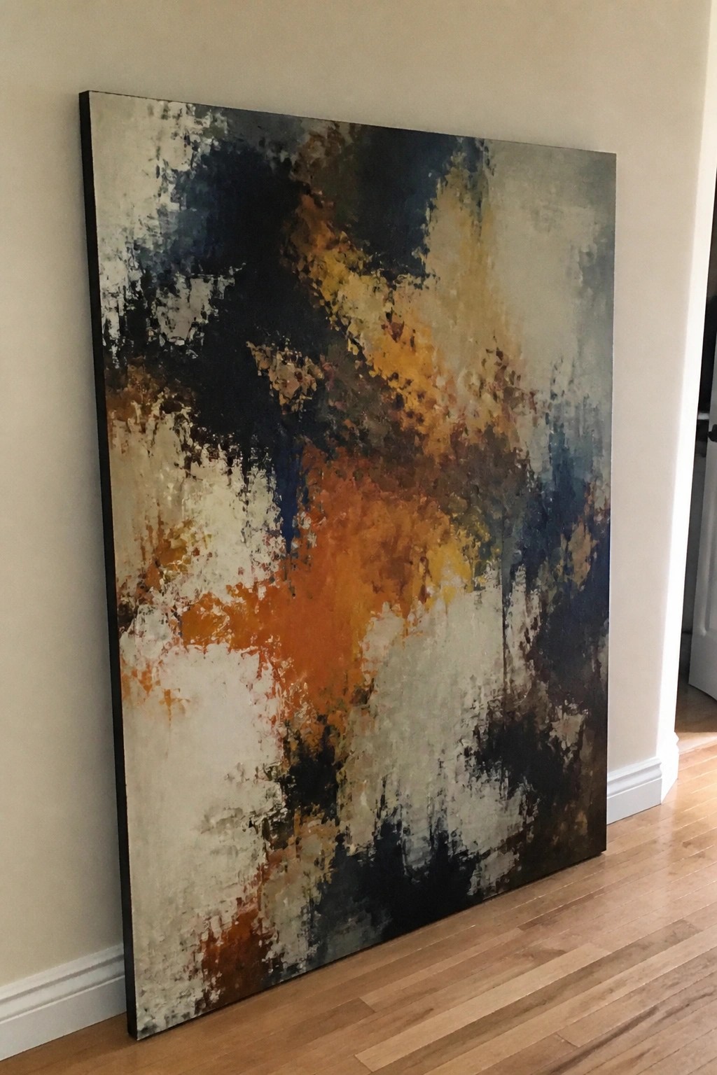 Large abstract painting with orange, navy, and beige brushstrokes leaning on wooden floor