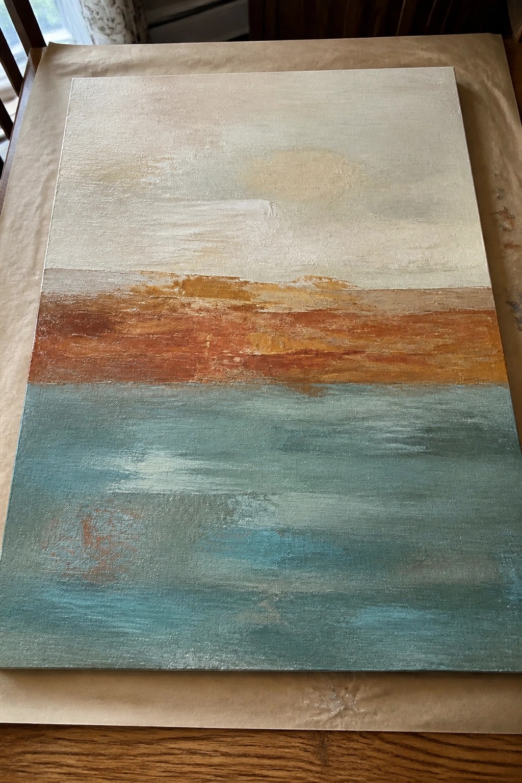 Abstract canvas painting with cream top, orange band, and teal bottom on paper.