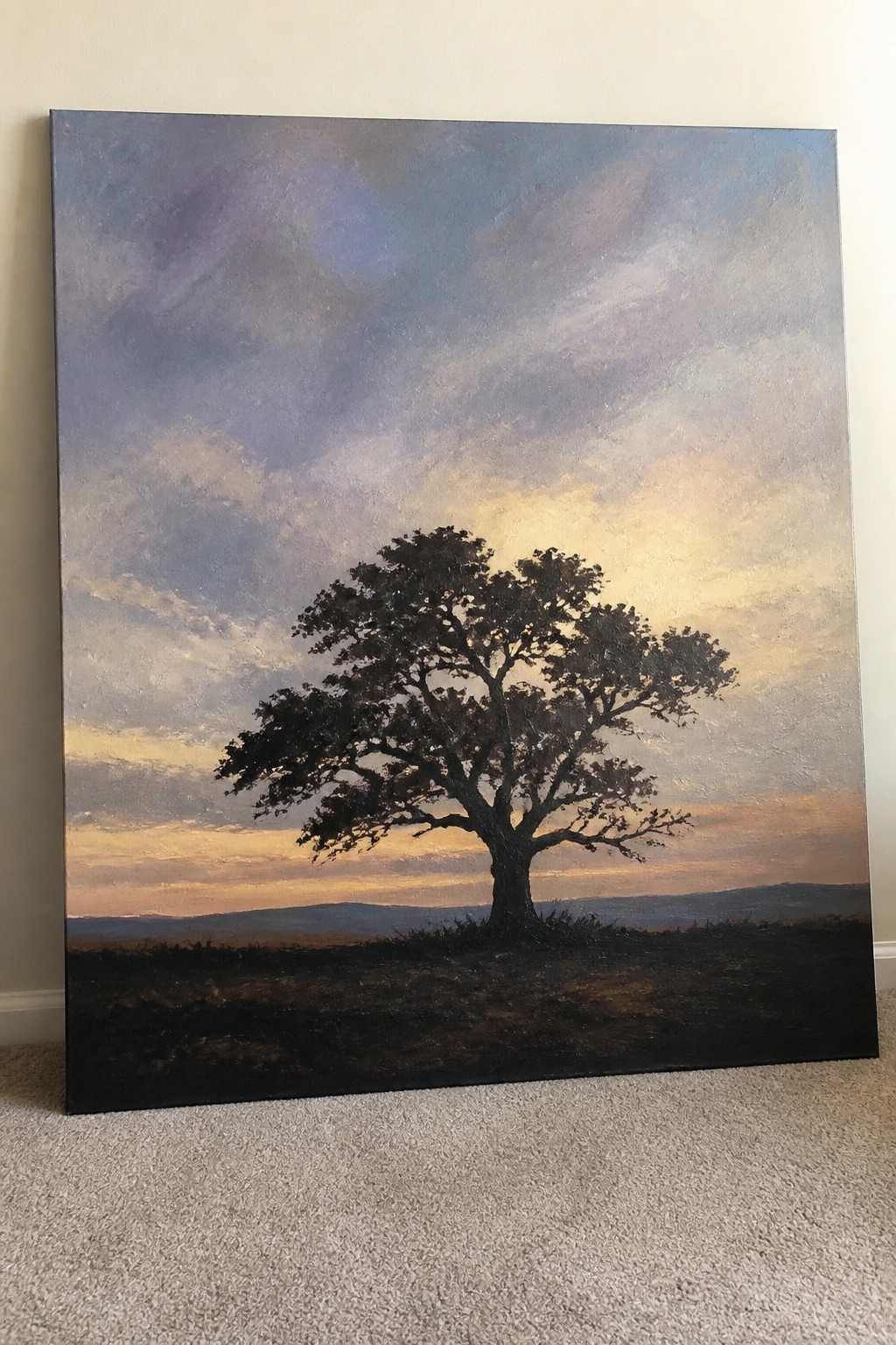 Lone tree silhouetted against vibrant sunset sky with purple and golden clouds over hills