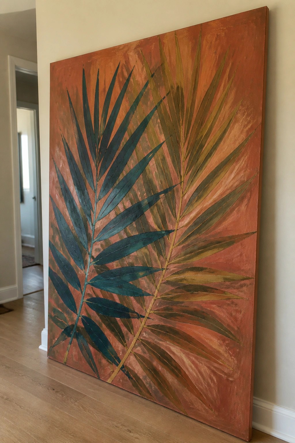 Large palm leaf painting with teal fronds on orange background leaning on wall