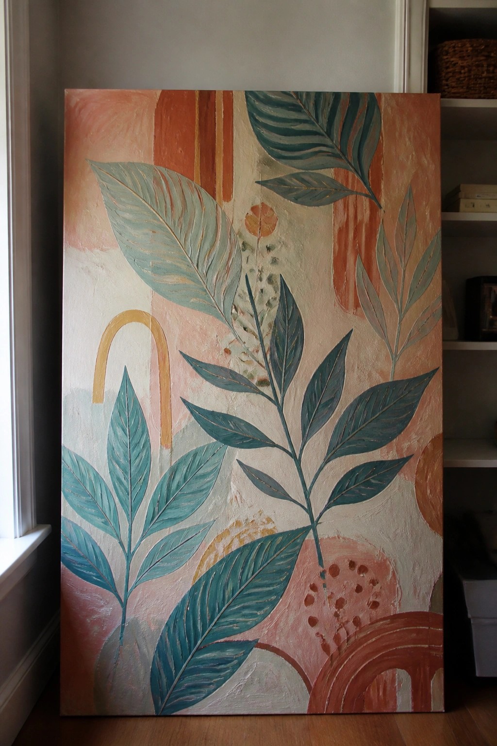 Abstract painting with teal leaves on coral and beige background leaning against wall