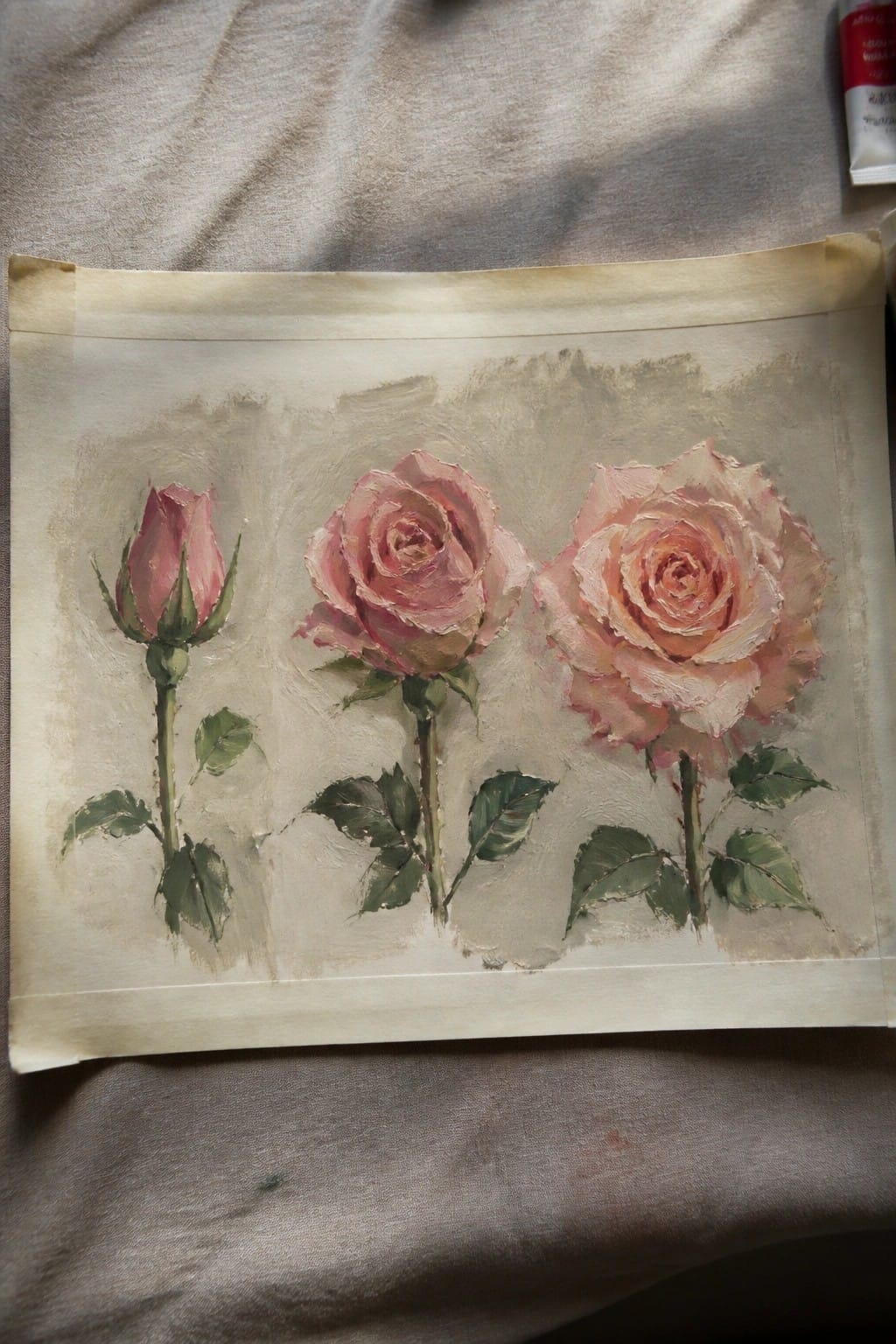 Three pink roses with green leaves painted on textured beige paper
