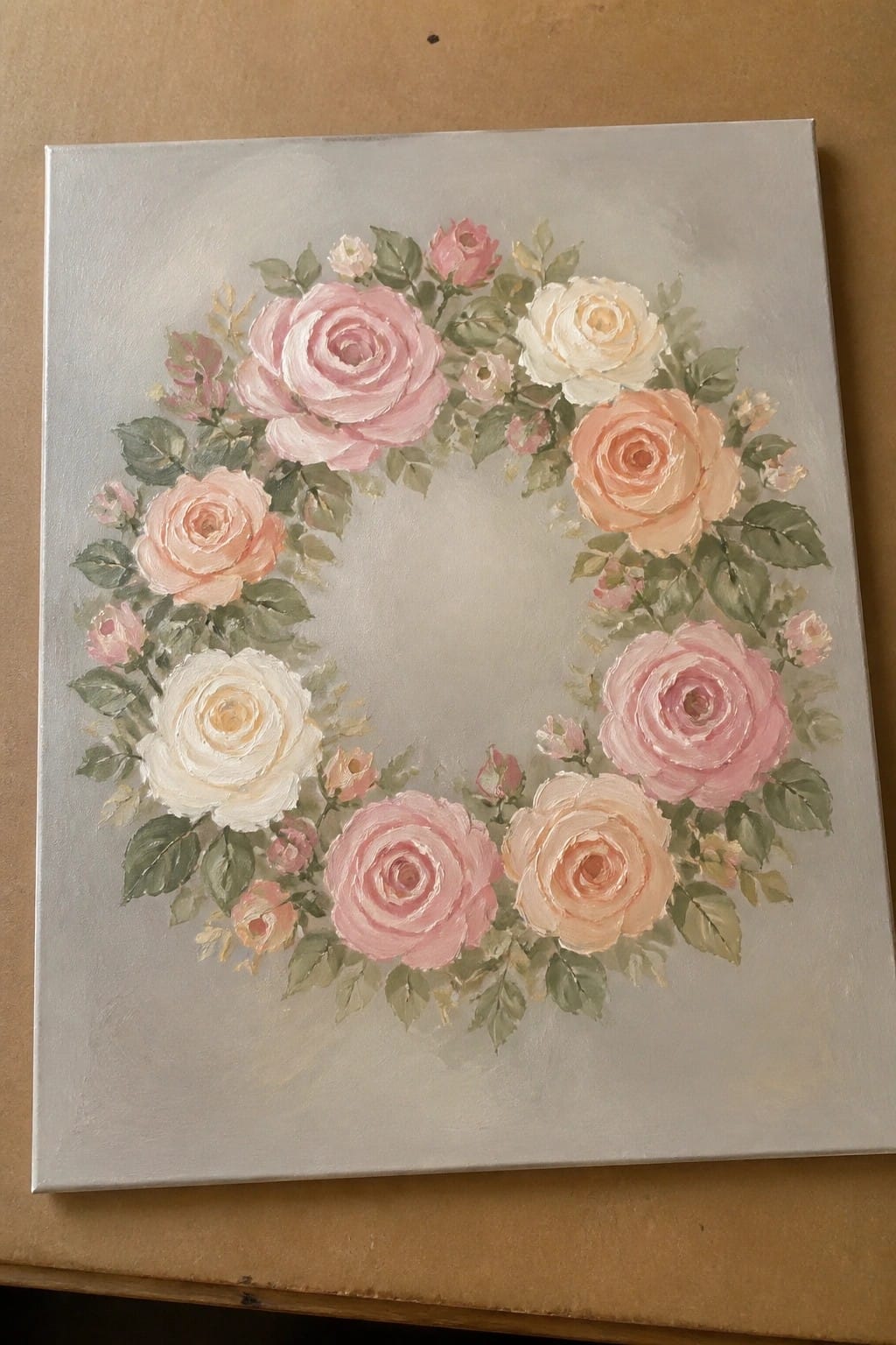 Circular wreath of pink, peach, and white roses with green leaves on a light gray canvas.