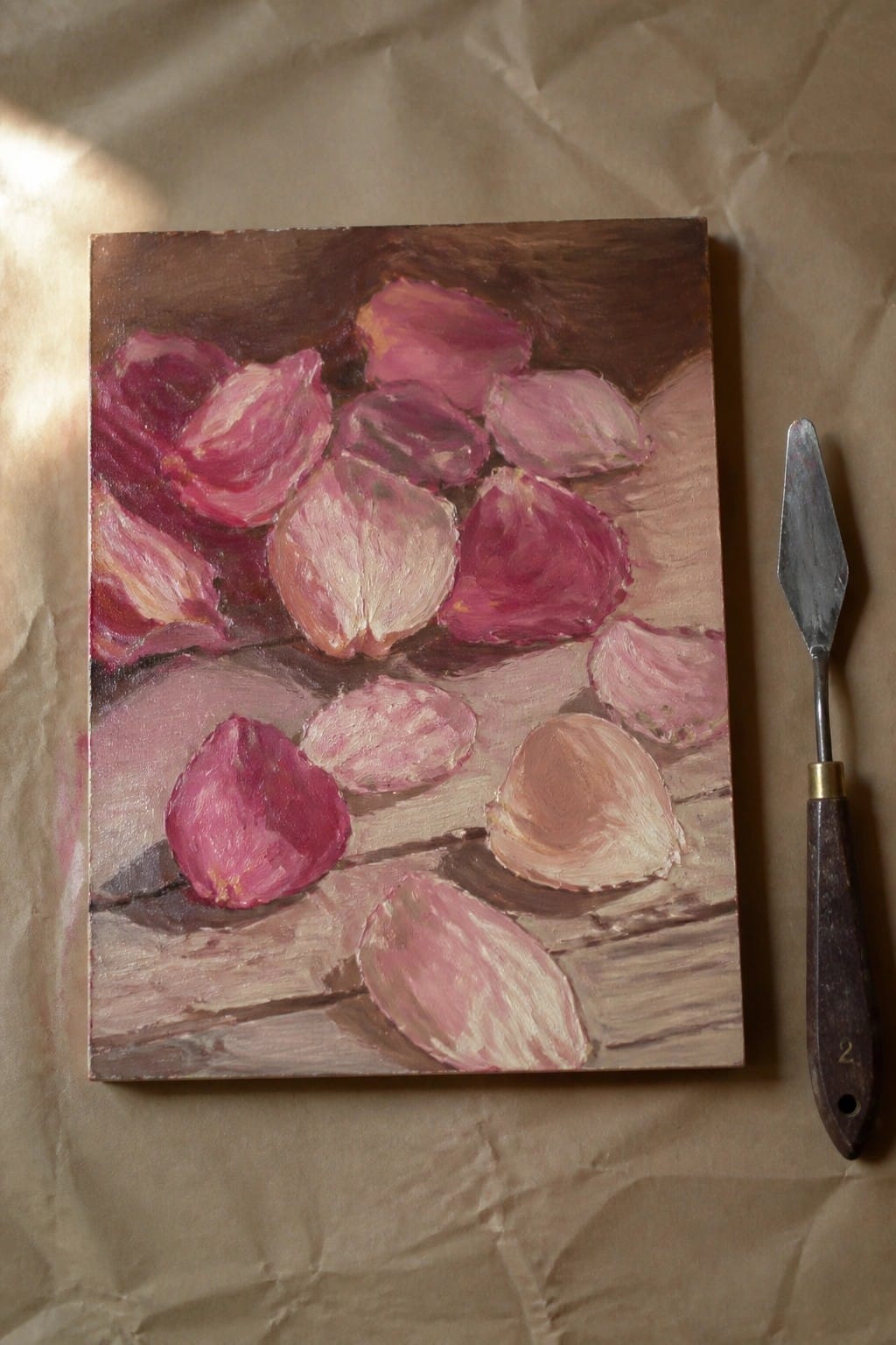 Painting of pink rose petals on wood beside palette knife on paper