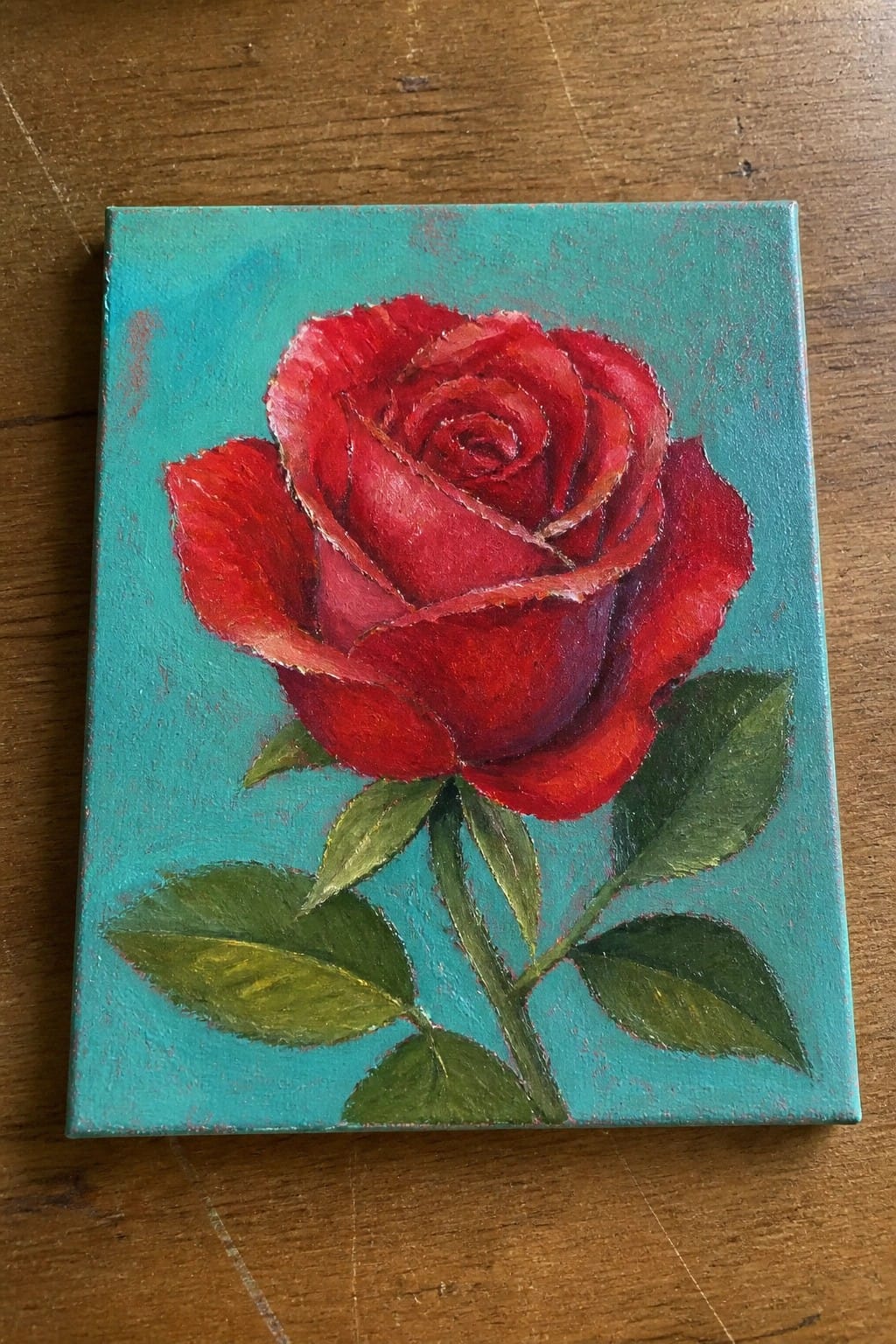 Vibrant red rose with green leaves on a textured teal canvas background