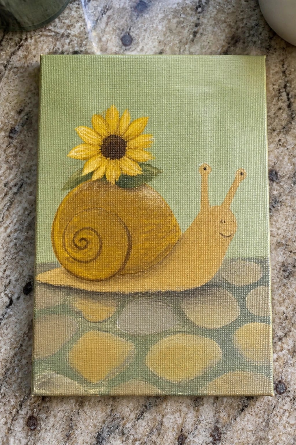 Yellow snail with sunflower on shell smiles atop green pebble path