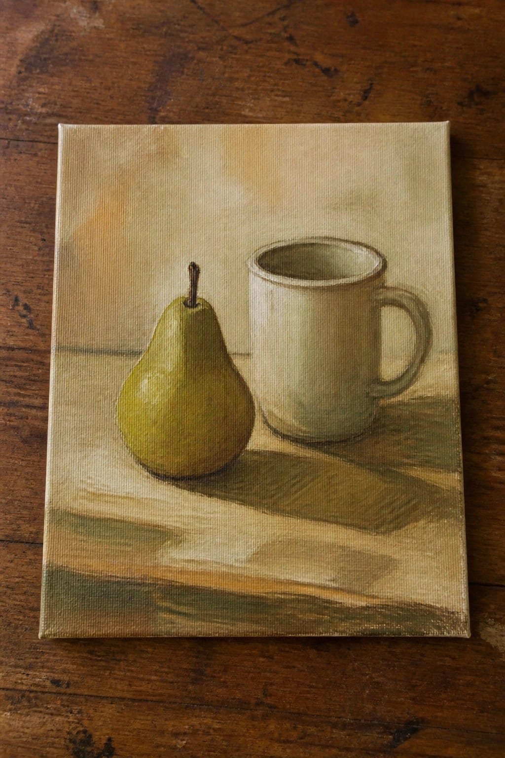 Green pear beside white mug in muted still life painting on wood.