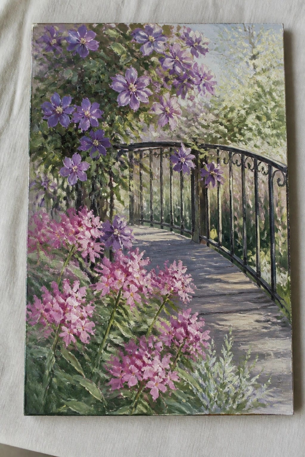 Curved wooden bridge with black railing amid lush purple and pink garden flowers.
