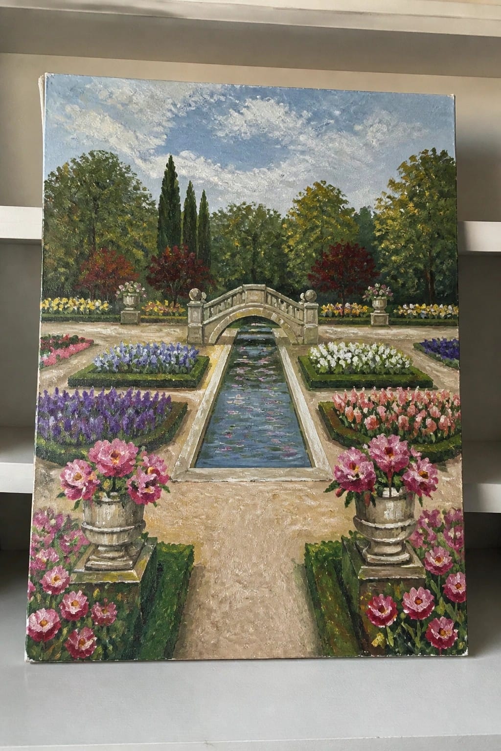 Formal garden painting with central canal, arched bridge, colorful flower beds, and urns.