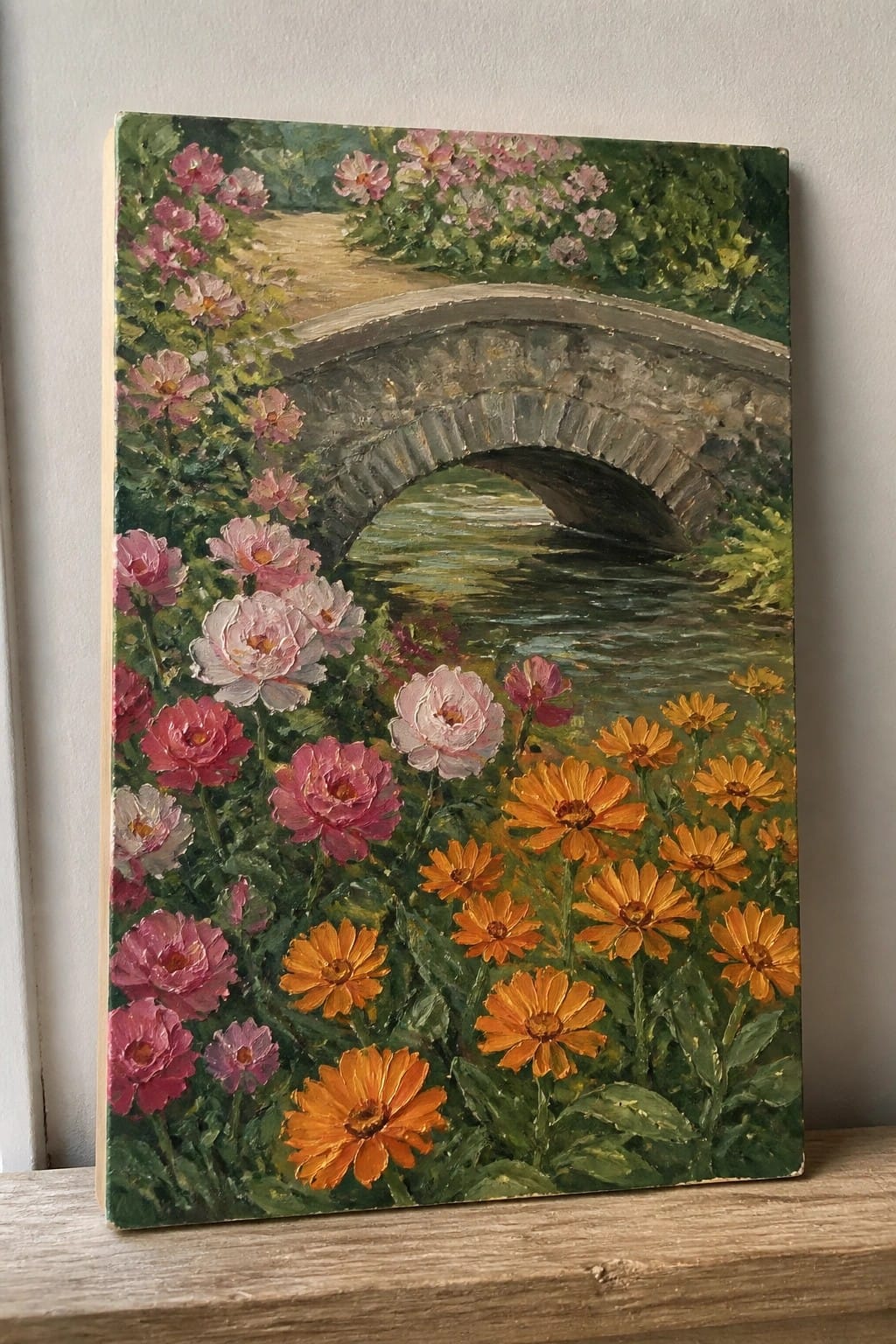 Stone arch bridge over stream amid lush pink roses and orange flowers.