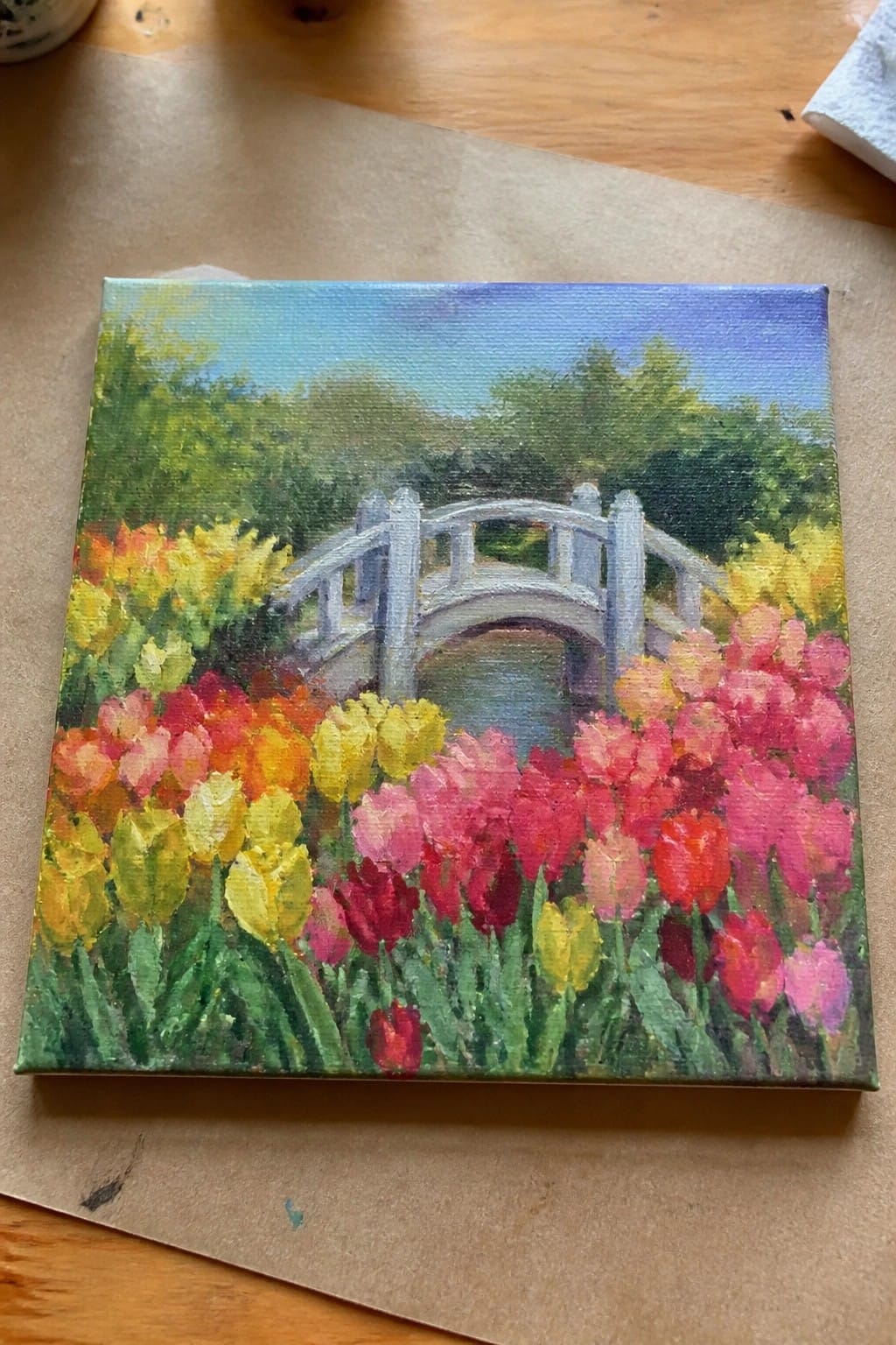 Vibrant painting of white bridge amid colorful pink yellow red tulips and green trees