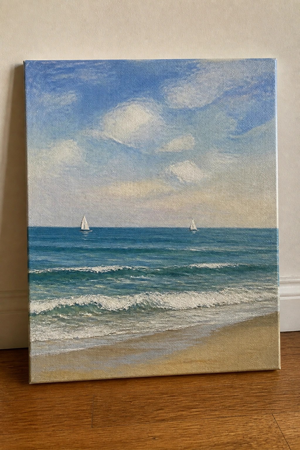 Realistic painting of beach with waves, sand, two sailboats on blue ocean under cloudy sky