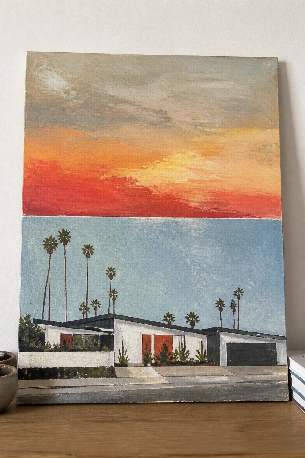 Painting of white mid-century house with palm trees under vibrant orange-red sunset sky.