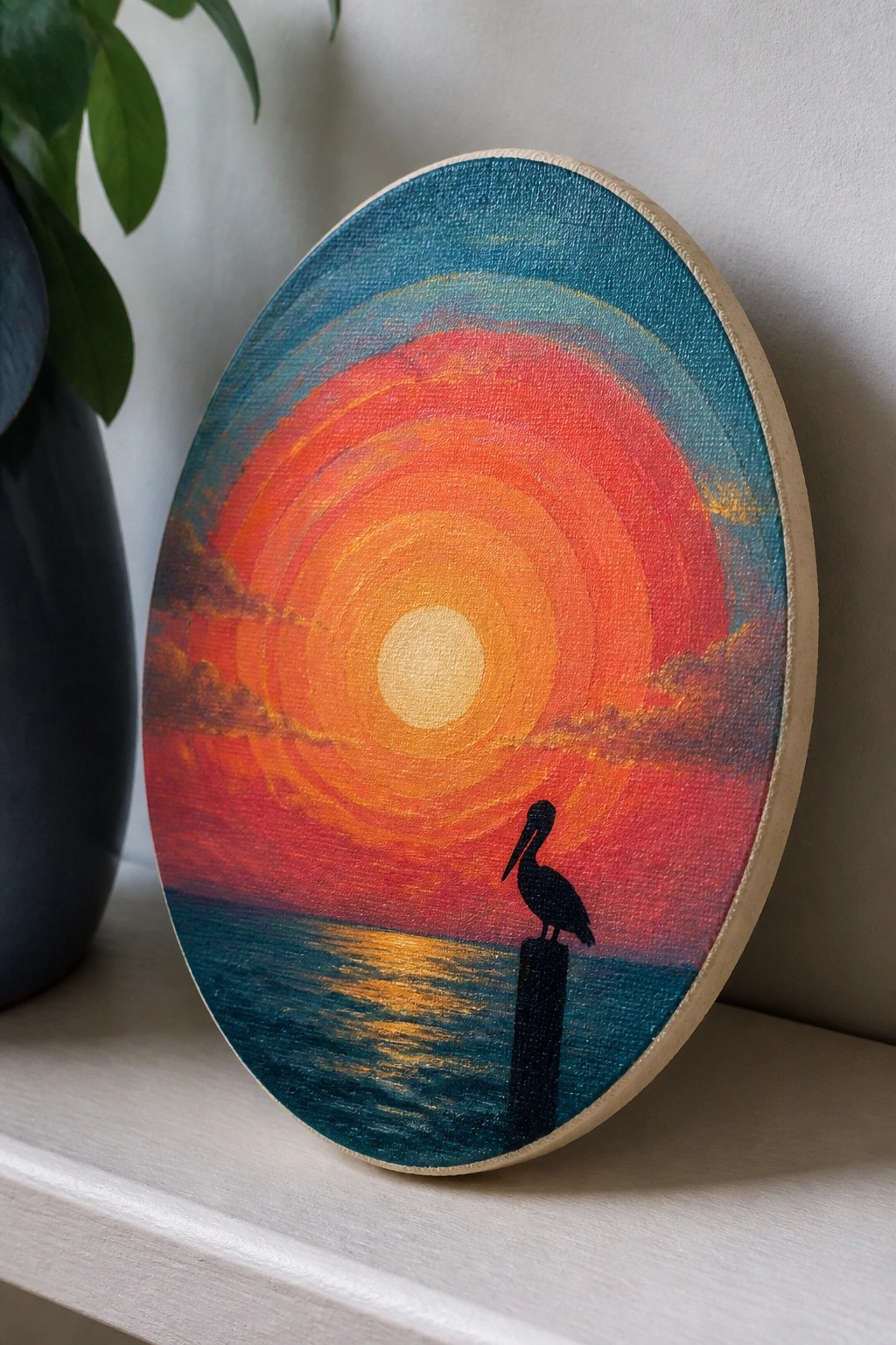 Circular canvas painting of vibrant sunset with silhouetted pelican on post over ocean