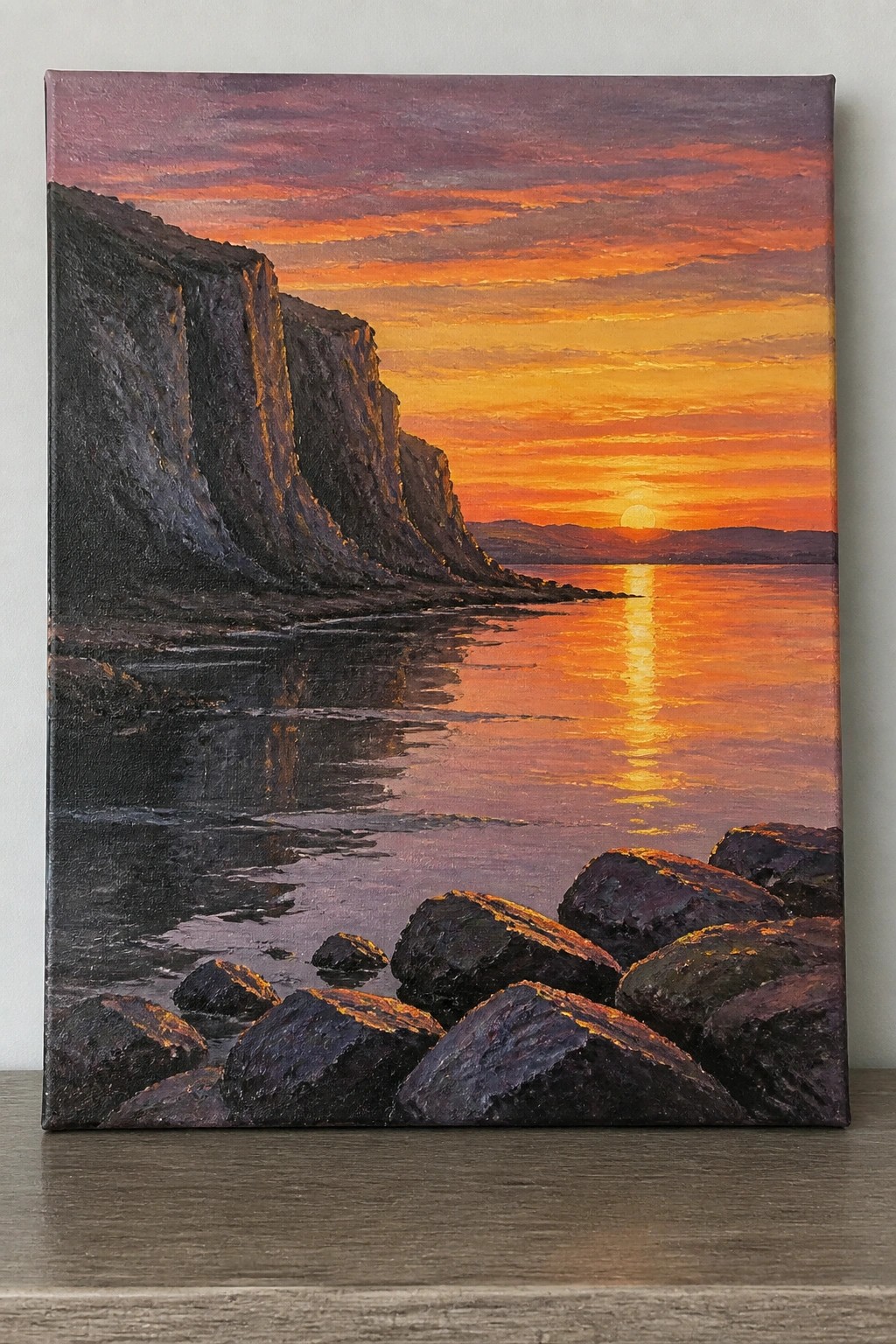Sunset painting with orange sky, cliffs, water reflections, and dark foreground rocks