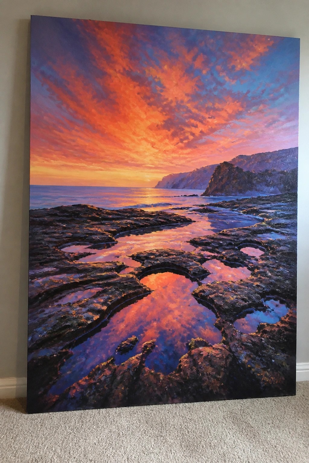 Vibrant sunset painting with fiery sky reflected in rocky coastal tide pools