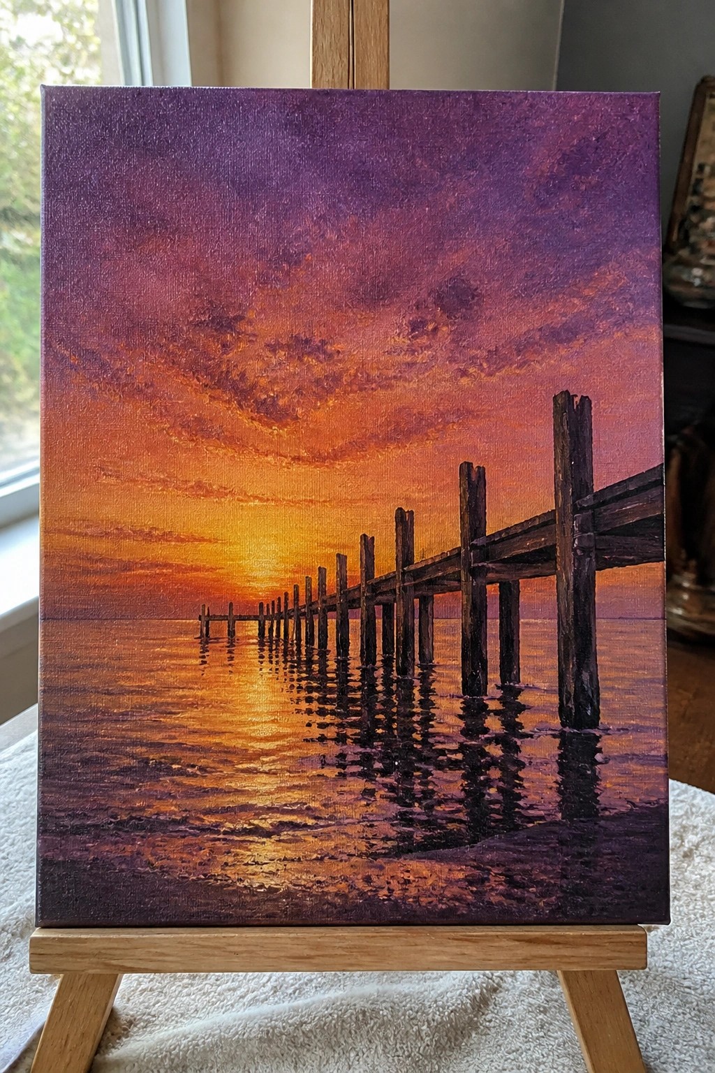 Vibrant sunset painting on easel with orange-purple sky and wooden pier over water