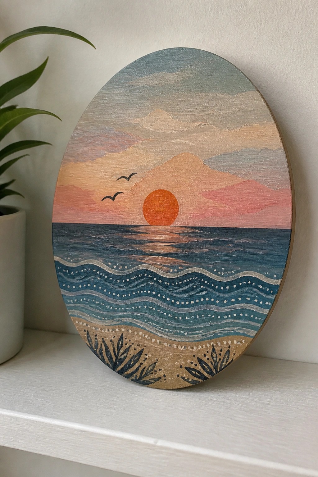 Oval wooden painting of sunset over ocean waves, mountains, and sandy shore.