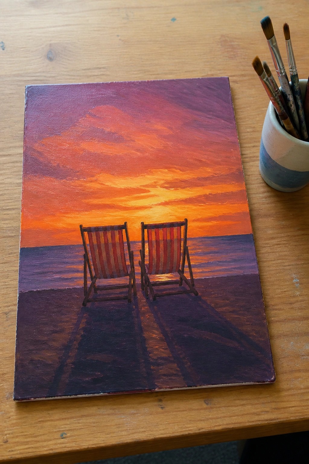 Two striped deck chairs on purple sand facing an orange sunset over the sea