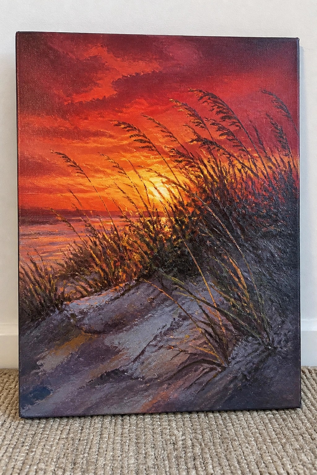 Fiery red-orange sunset painting over water with windblown tall grasses on dunes.