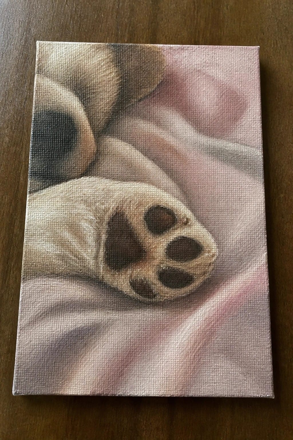 Close-up painting of a dog's light paw with dark pads on pink fabric