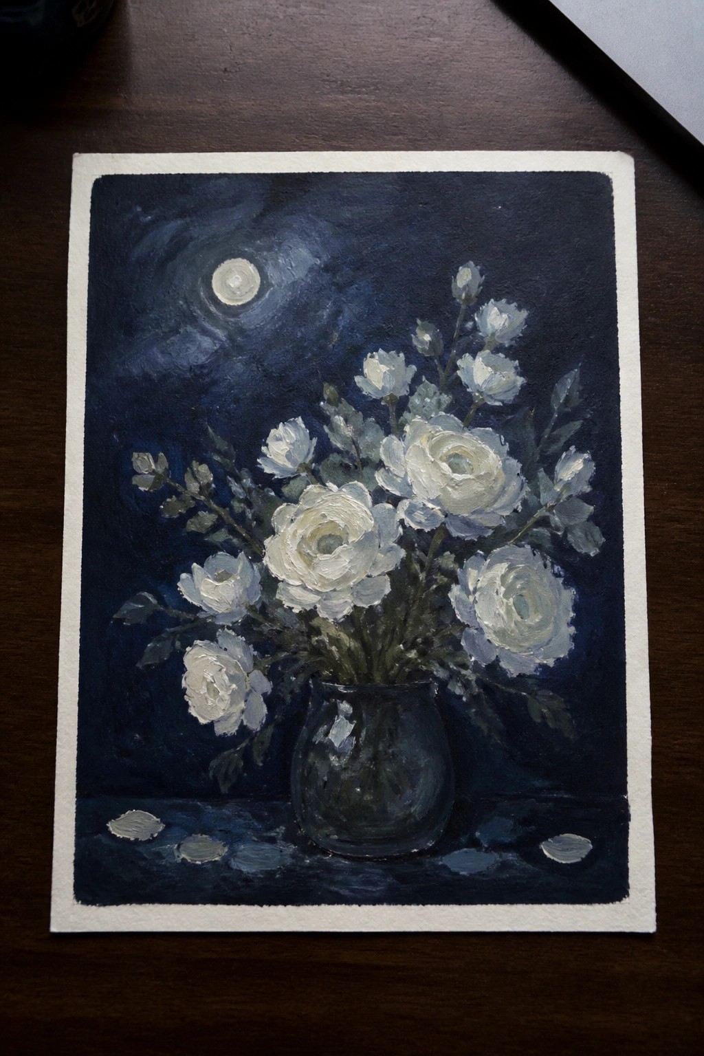 White roses in glass vase beneath moon in swirling dark blue night sky with petals.