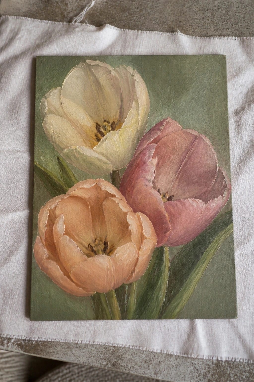 Three tulips in cream, pink, and peach painted on green canvas.