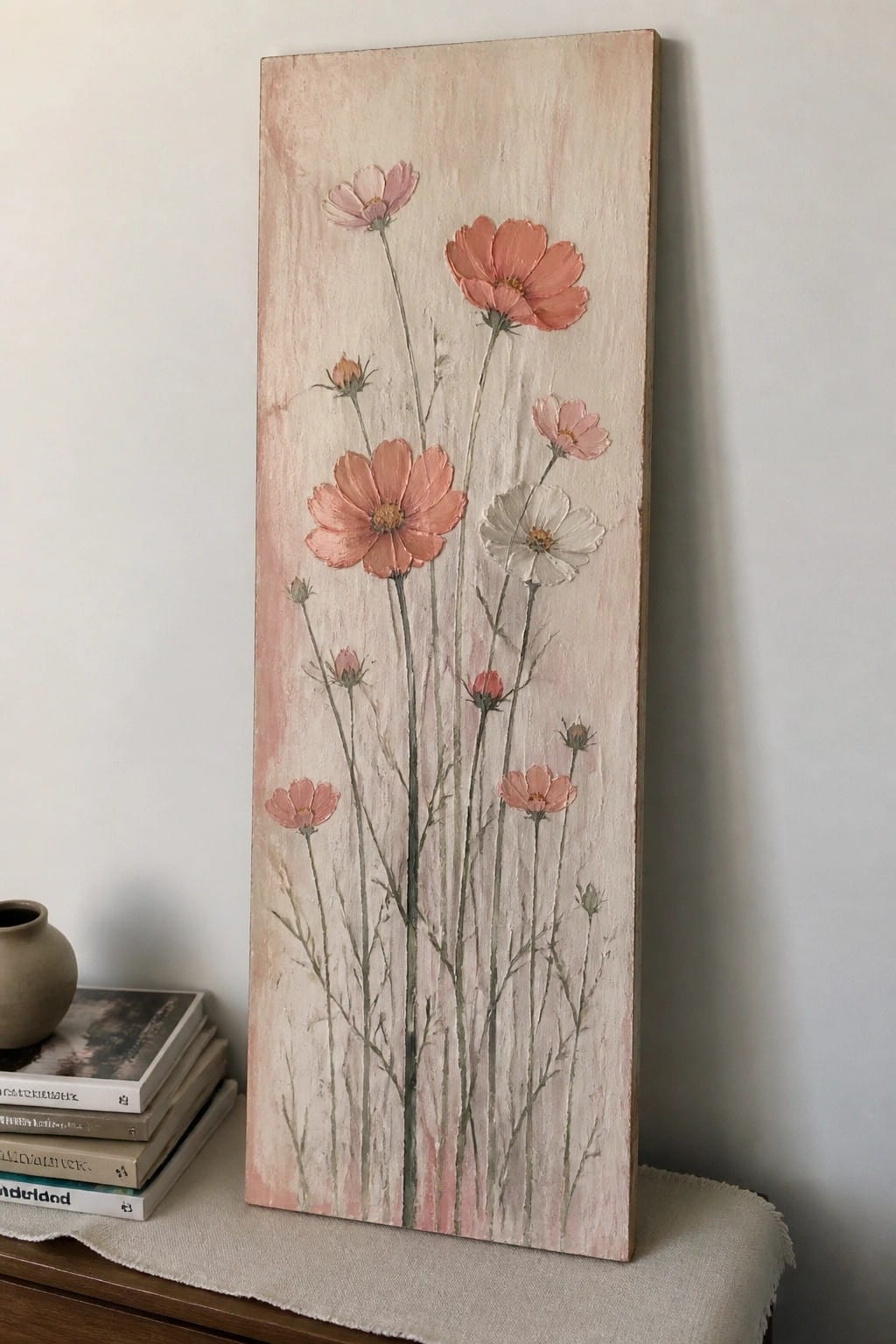 Tall canvas with pink cosmos flowers beside stacked books and a vase.