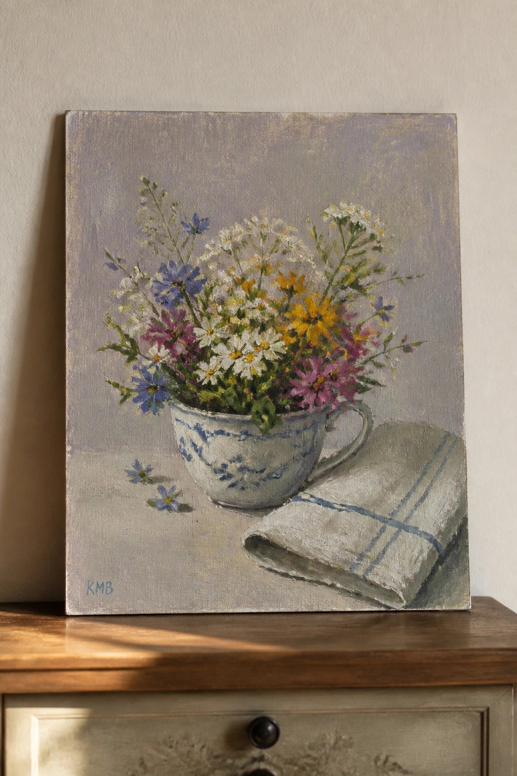 Impressionistic painting of colorful wildflowers in a blue-patterned teacup beside a cloth.