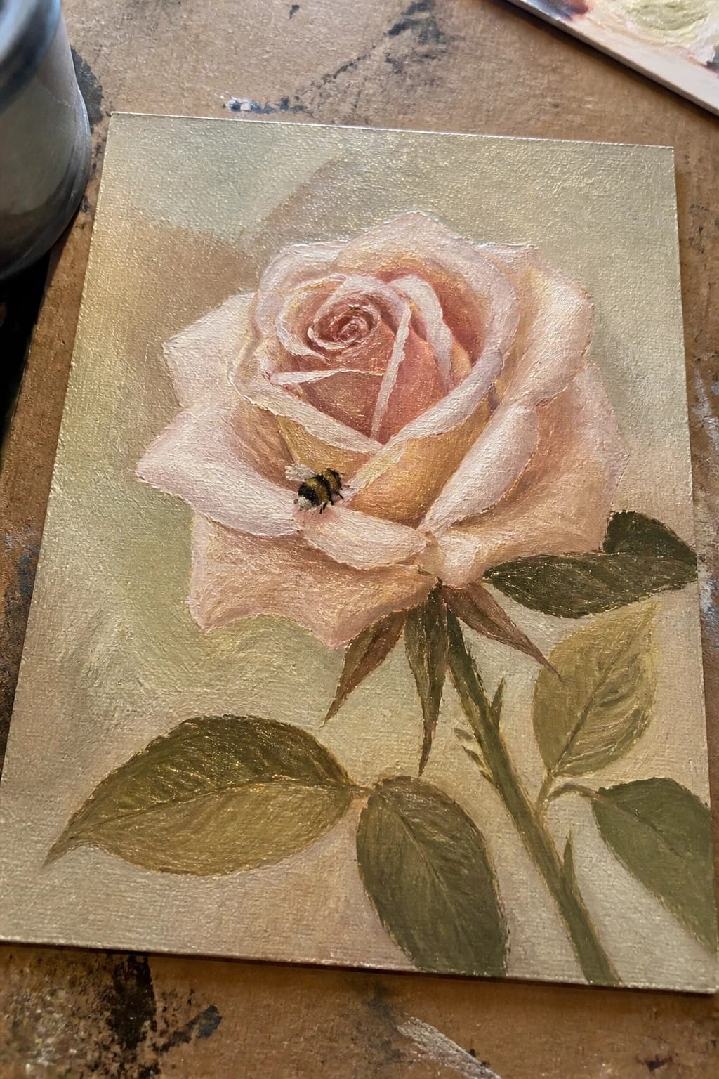 Blooming pink rose with bumblebee on petal, golden background, green leaves and stem