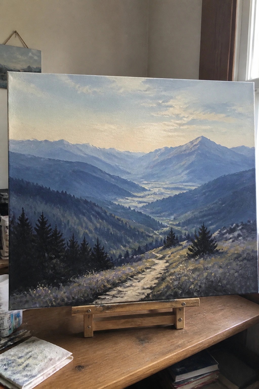 Oil painting of blue mountain valley with winding path on wooden easel