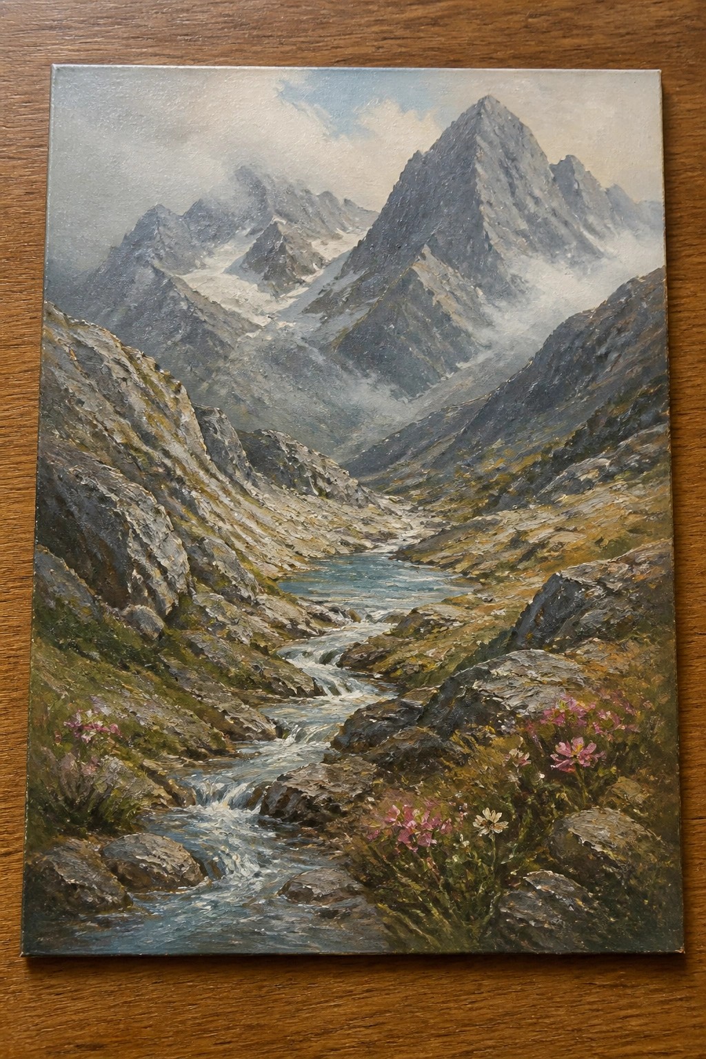 Oil painting of misty mountains with river, rocks, and pink wildflowers in valley.