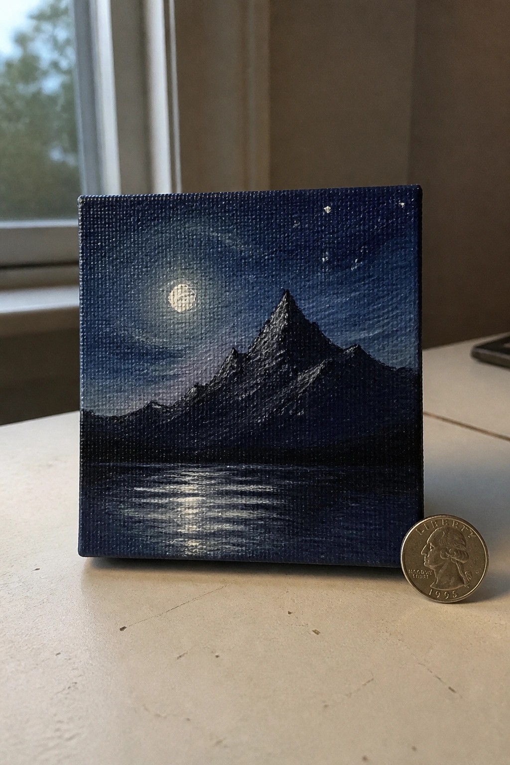Small canvas night painting of moon, stars, mountains reflected in water beside quarter coin