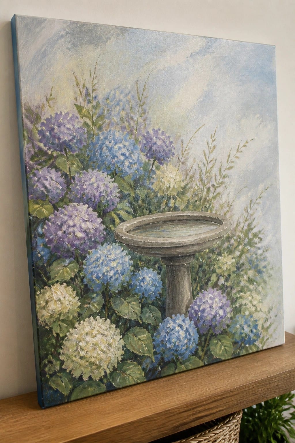 Canvas painting of purple and blue hydrangeas surrounding a stone birdbath.