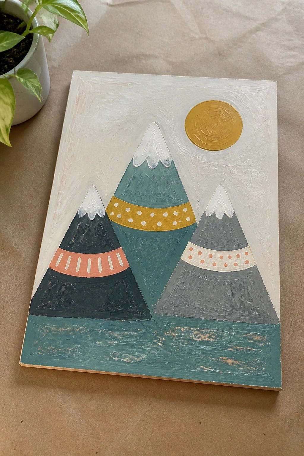 Abstract painting of three geometric mountains with patterned bands and a yellow sun.