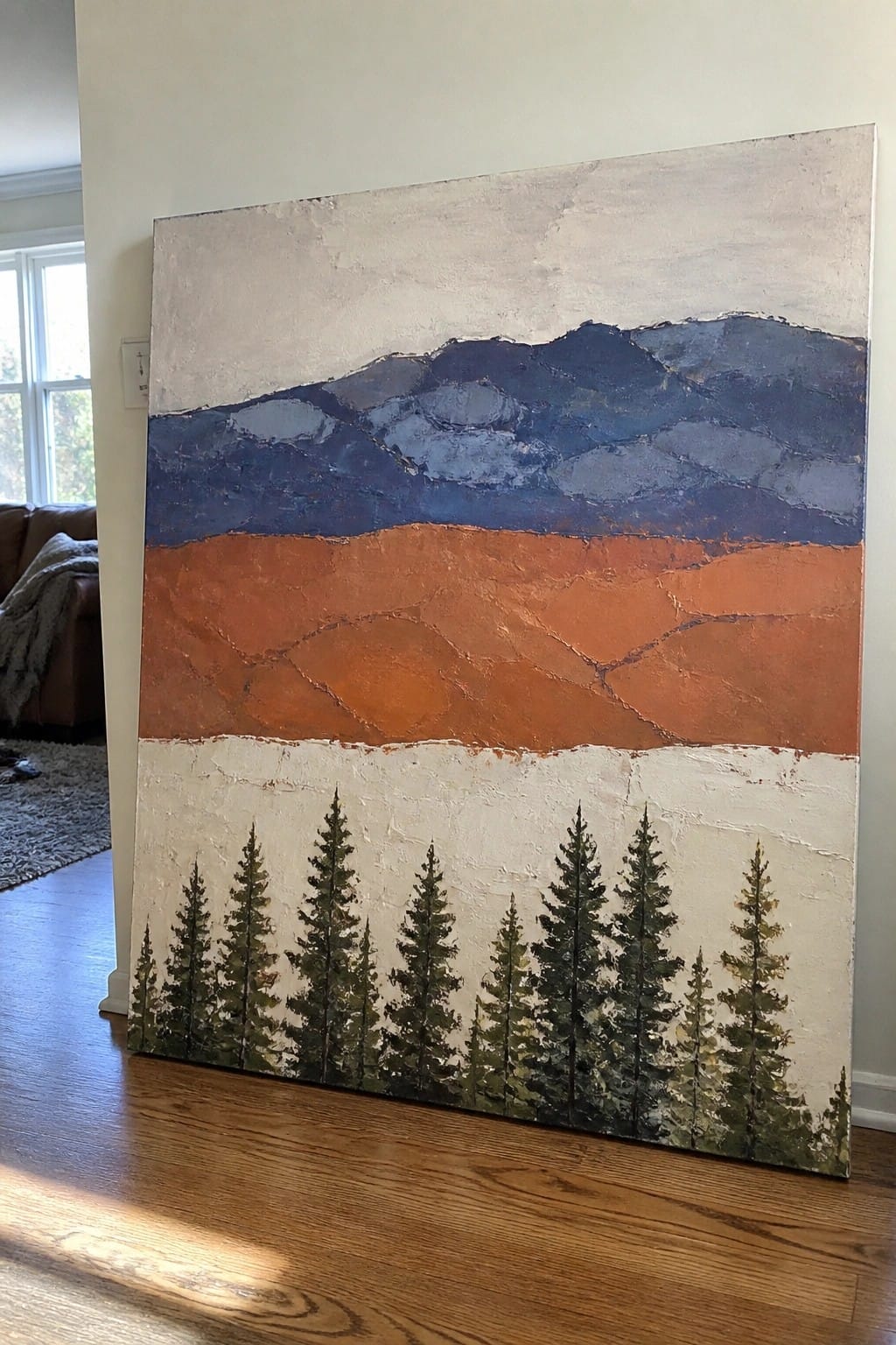 Abstract landscape painting with blue mountains, orange field, and green pine trees on canvas.