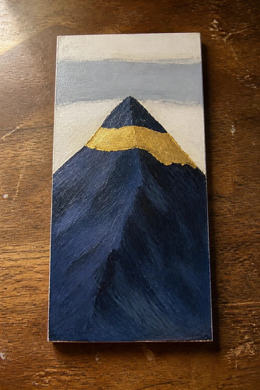 Abstract mountain painting with dark blue slopes, gold band, and white peak on canvas