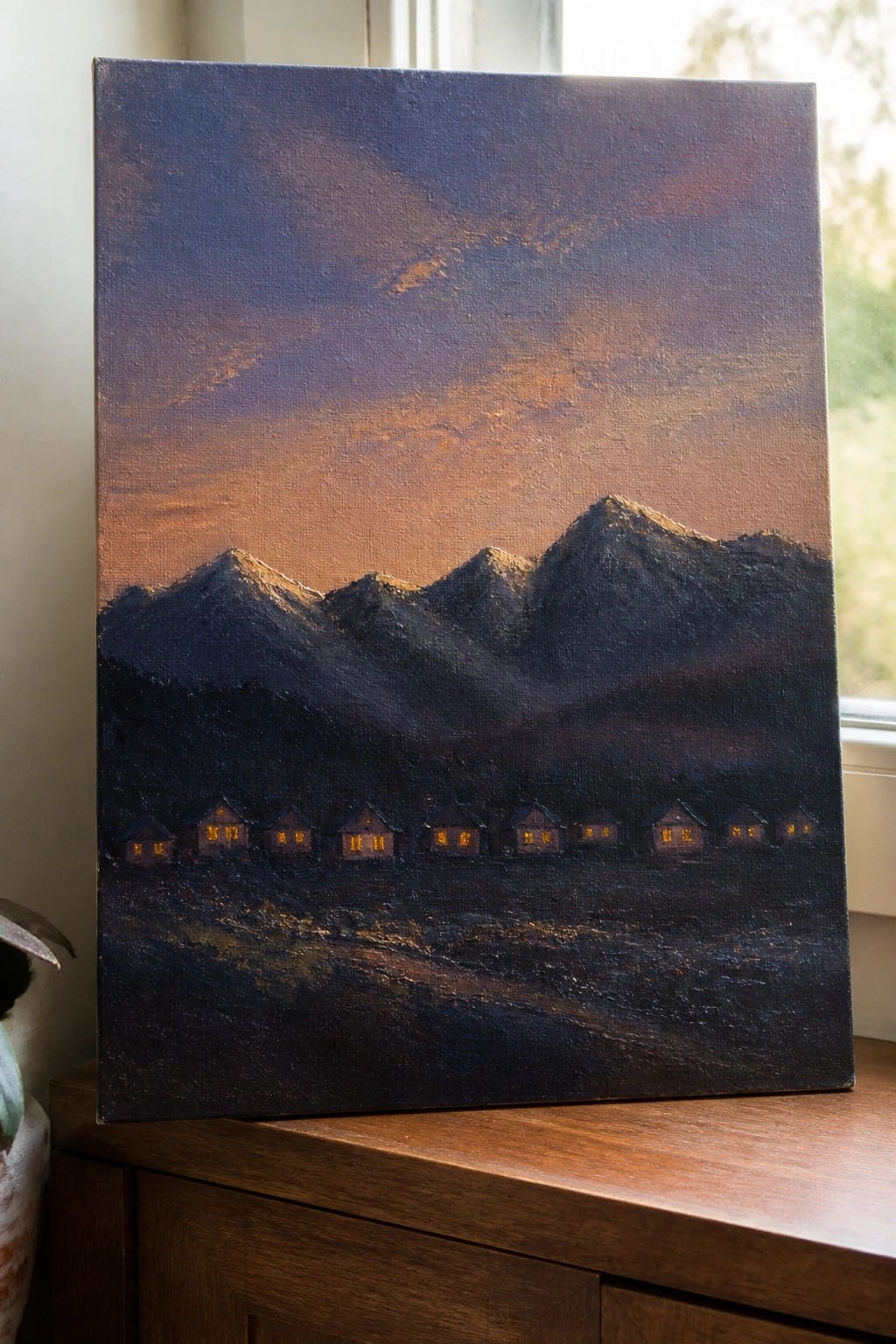 Textured painting of glowing houses at the foot of dark mountains under a purple-orange sky.